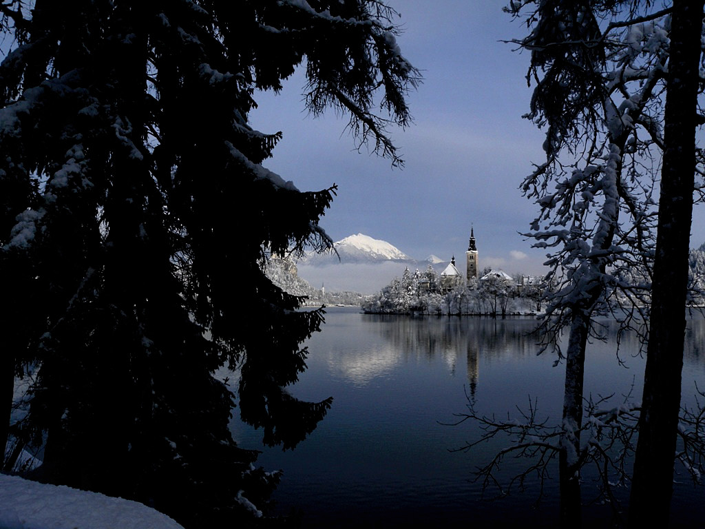Fresh snow covered landscape, the tiny island with a quaint chapel and the cliff overlooking the village Lake Bled in Winter